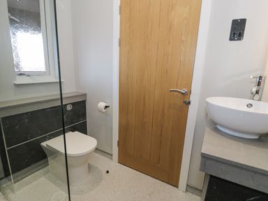 A bathroom with a toilet, wooden door, white vessel sink on countertop, and frosted window at Luxury Lodge 46 in Dyserth