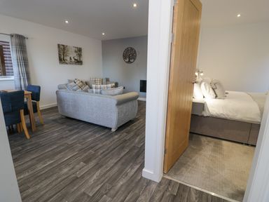A living room with gray sofas and a dining table next to a bedroom with a bed at Luxury Lodge 46 in Dyserth