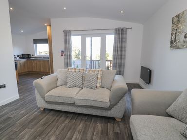 A living room with two beige sofas a glass door with grey plaid curtains and a view into a kitchen at Luxury Lodge 53 in Dyserth