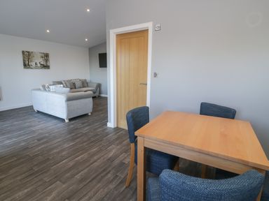 A dining table with four chairs and a seating area with two sofas and a wall painting at Luxury Lodge 53 in Dyserth