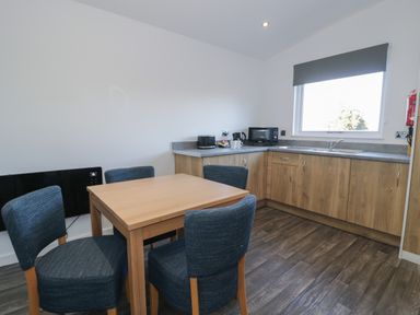 A kitchen with a wooden table and four blue chairs a microwave toaster kettle and sink by a window at Luxury Lodge 53 in Dyserth