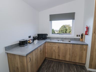 A kitchen with wooden cabinets a gray countertop a microwave toaster kettle mugs and a window with a view at Luxury Lodge 53 in Dyserth