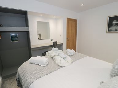 A bedroom with a bed, folded towels, a vanity desk with a chair, a mirror, wooden door, and framed picture on the wall at Luxury Lodge 53 in Dyserth