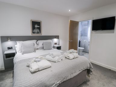 A bedroom with a bed arranged with pillows robes and towels an open door showing a bathroom and a wall mounted television at Luxury Lodge 53 in Dyserth