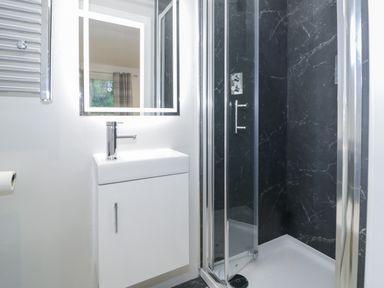 A bathroom with a white sink cabinet a lit mirror and a shower with black walls and glass doors at Luxury Lodge 53 Dyserth