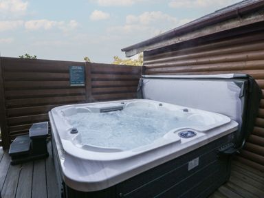 An outdoor hot tub with bubbling water next to a wooden cabin and fence at Luxury Lodge 53 in Dyserth