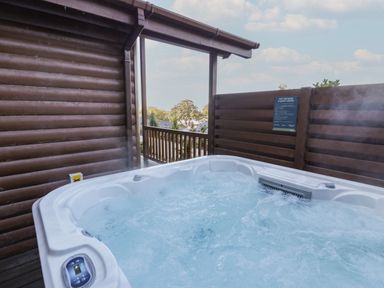 An outdoor hot tub next to a wooden cabin with a safety notice on a wooden fence at Luxury Lodge 53 Dyserth