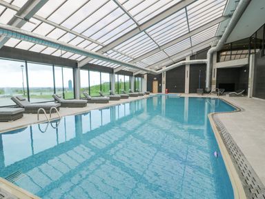 An indoor swimming pool with lounge chairs along the glass wall at Luxury Lodge 62 in Dyserth