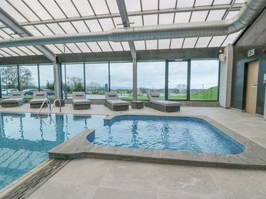 An indoor pool area with lounge chairs and large windows showing an outdoor landscape at Luxury Lodge 62 in Dyserth