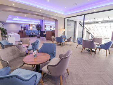 A lounge area with round tables and blue and gray chairs under purple ceiling lights at Luxury Lodge 62 in Dyserth