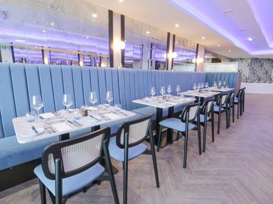 A dining area with tables set with glasses and cutlery alongside blue upholstered bench seating and chairs at Luxury Lodge 62 in Dyserth