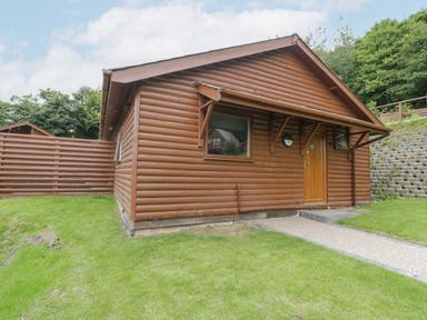 A wooden cabin with a pathway leading to the door and grass surrounding it at Luxury Lodge 62 in Dyserth