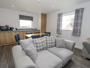 A living room with a gray sofa and pillows beside a dining table and kitchen area with wooden cabinets at Luxury Lodge 62 in Dyserth