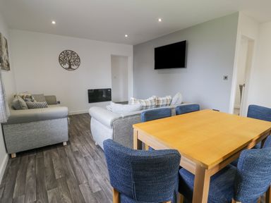 A living room with two gray sofas a wooden dining table with blue chairs and a wall-mounted television at Luxury Lodge 62 in Dyserth
