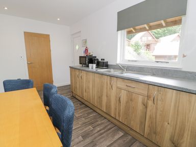 A kitchen with wooden cabinets countertop sink microwave kettle toaster dining table and blue chairs at Luxury Lodge 62 in Dyserth