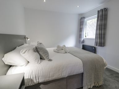 A bedroom with a bed with white sheets gray pillows and a gray blanket near a window with gray curtains at Luxury Lodge 62 in Dyserth