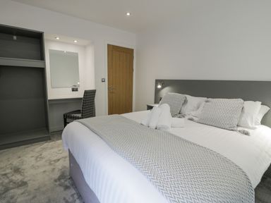 A bedroom with a double bed pillows blankets a chair desk mirror and open wardrobe at Luxury Lodge 62 in Dyserth