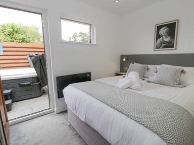 A bedroom with a double bed and rolled towels next to an open door leading to an outdoor hot tub at Luxury Lodge 62 in Dyserth