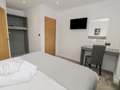 A bedroom with a bed, towels, an open wardrobe, a wooden door, a wall-mounted TV, a desk with a mirror, and a checked chair at Luxury Lodge 62 Dyserth