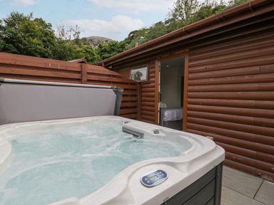An outdoor hot tub beside a wooden lodge with a door open to a bedroom at Luxury Lodge 62 in Dyserth