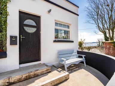 An exterior entrance with a black door and a window next to a light blue bench by a curved wall at The Old Coastguard Tower Buncrana County Donegal