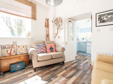 A living room with a beige sofa with nautical cushions and a wooden chest near a window with bamboo blinds at The Old Coastguard Tower Buncrana Buncrana County Donegal