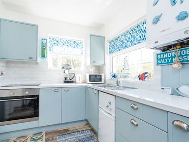 A kitchen with blue cabinets white countertop oven microwave and sink at The Old Coastguard Tower Buncrana in Buncrana County Donegal