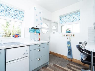 A kitchen with blue cabinets white countertops a small refrigerator and a seating area with stools at The Old Coastguard Tower Buncrana in Buncrana County Donegal