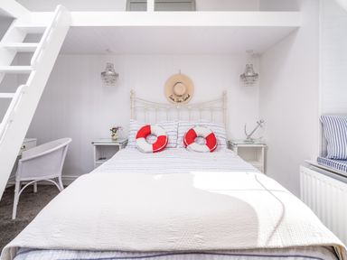A bedroom with a bed with striped bedding and two red and white round pillows two bedside tables with lamps and decorations a white chair and a white ladder leading to a loft at The Old Coastguard Tower Buncrana in Buncrana County Donegal