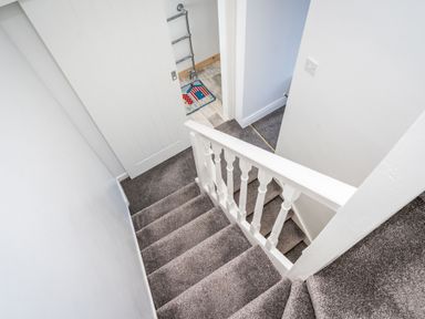 A stairway with grey carpet and white railing leading down to a landing with a partially open white door and a floor mat at The Old Coastguard Tower Buncrana in Buncrana County Donegal