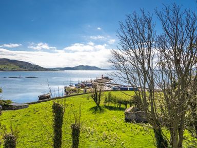 A view of a harbor with boats docked near a pier by green fields and trees at The Old Coastguard Tower Buncrana in Buncrana County Donegal