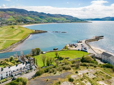 A coastal area with houses green fields a golf course a pier with parked cars and boats at The Old Coastguard Tower Buncrana in Buncrana County Donegal