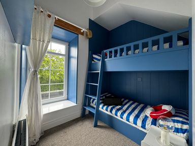 A small bedroom with blue bunk beds striped bedding a window with white curtains and a small bedside table with a lamp at The Old Coastguard Tower Buncrana in Buncrana County Donegal