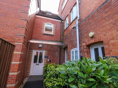 A brick building entrance with a white door and green plants nearby at The Lobster Pot in Weymouth