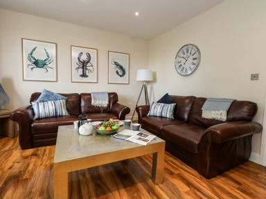 A living room with two brown leather sofas a coffee table with fruit and tea set and wall art at The Lobster Pot in Weymouth