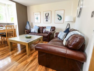 A living room with brown leather sofas a wooden coffee table and framed pictures of sea creatures on the wall at The Lobster Pot in Weymouth
