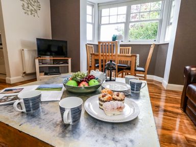 A living room with a coffee table set for tea with mugs pastries and fruit at The Lobster Pot in Weymouth