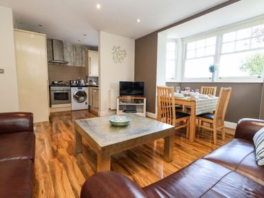A living room with brown leather sofas a square coffee table and a small dining table set near windows at The Lobster Pot in Weymouth