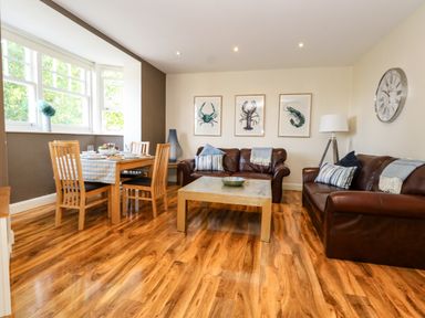 A living room with two brown leather sofas a wooden dining table with chairs and framed sea creature prints on the wall at The Lobster Pot in Weymouth