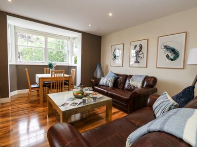 A living room with brown leather sofas a wooden dining table and lobster artwork on the wall at The Lobster Pot in Weymouth