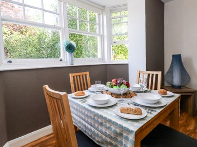 A dining table with plates glasses bread and a fruit bowl next to windows and a decorative lamp at The Lobster Pot in Weymouth