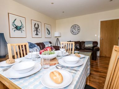 A dining table set with plates bowls bread and glasses in a living room with leather sofas framed sea creature prints and a clock on the wall at The Lobster Pot in Weymouth