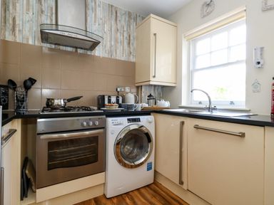 A kitchen with a stove oven washing machine countertop sink and window at The Lobster Pot in Weymouth