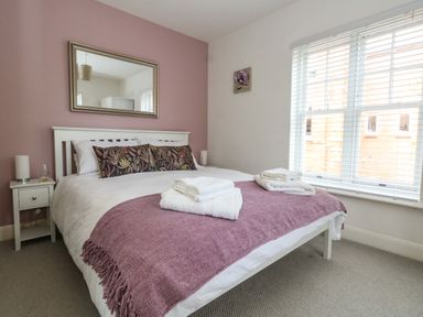 A bedroom with a white bed and purple throw blanket beside a window at The Lobster Pot in Weymouth