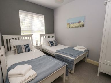 A bedroom with two single beds, blue striped cushions, blue throws, a bedside table with lamps, and a wardrobe at The Lobster Pot in Weymouth