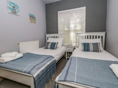 A bedroom with two single beds with blue blankets and striped pillows with a window between the beds at The Lobster Pot in Weymouth