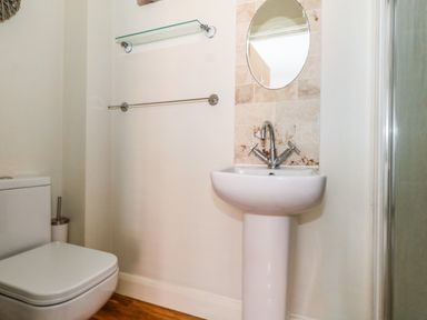 A bathroom with a toilet, pedestal sink with a round mirror above, towel rail, and glass shelf at The Lobster Pot in Weymouth