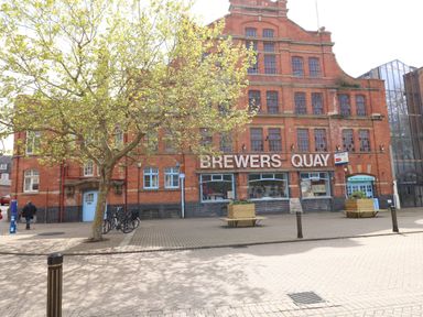 A red brick building with the sign Brewers Quay and trees and benches outside at The Lobster Pot in Weymouth