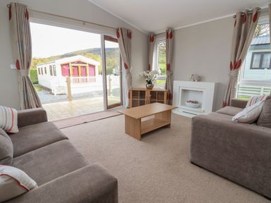 A living room with two sofas a coffee table a cabinet and a sliding glass door at Lodge 4 in St Asaph