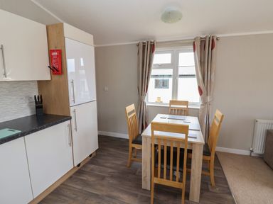 A dining area with a wooden table and four chairs next to a window with curtains in a kitchen space at Lodge 4 in St Asaph